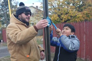 Bearded man in a hat and elementary school kid attach trail marker to street sign